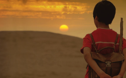 picture of a boy looking over hills with a setting or rising sun.