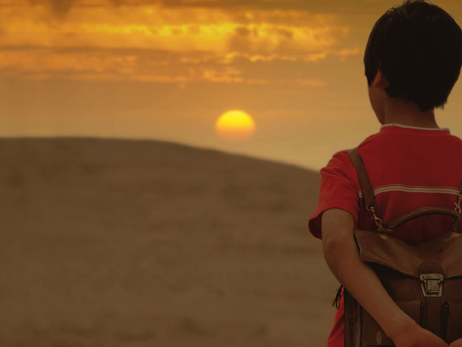 picture of a boy looking over hills with a setting or rising sun.
