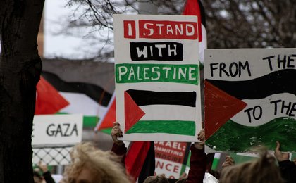 Someone at a rally holding a sign that reads 'I stand with Palestine'. Other people are also holding signs in support of Palestine