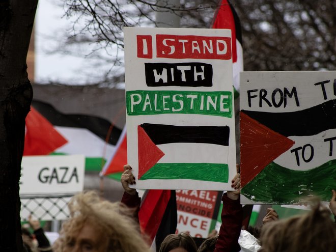 Someone at a rally holding a sign that reads 'I stand with Palestine'. Other people are also holding signs in support of Palestine